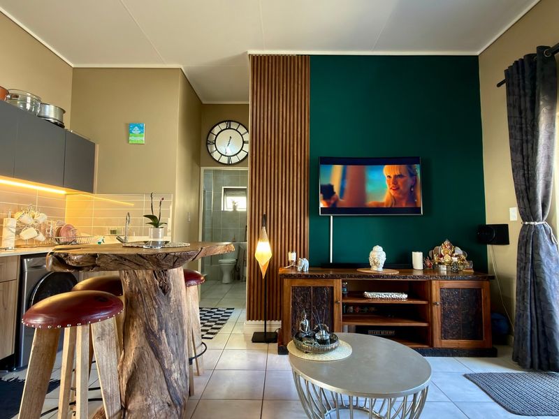 Modern open-plan living area featuring a sleek kitchen with built-in cabinetry, a striking green feature wall with wood paneling, and tiled flooring throughout.