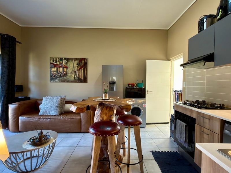 Modern open-plan living area featuring a well-equipped kitchen with built-in cabinetry, gas hob, and tiled flooring, seamlessly flowing into the lounge space.