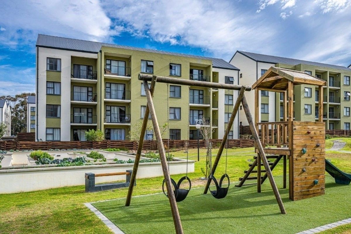 Exterior view of an apartment complex featuring a communal playground, landscaped garden beds, and private balconies.