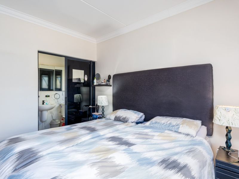 A well-maintained bedroom featuring crown molding and direct access to an en-suite bathroom through a modern sliding glass door.