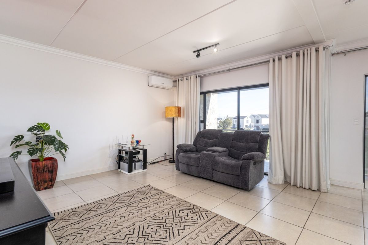 A bright living room featuring neutral tiled flooring, a split-system air conditioner, and a large sliding glass door providing access to the balcony.