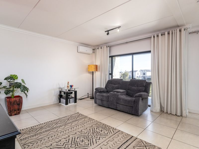 A bright living room featuring neutral tiled flooring, a split-system air conditioner, and a large sliding glass door providing access to the balcony.