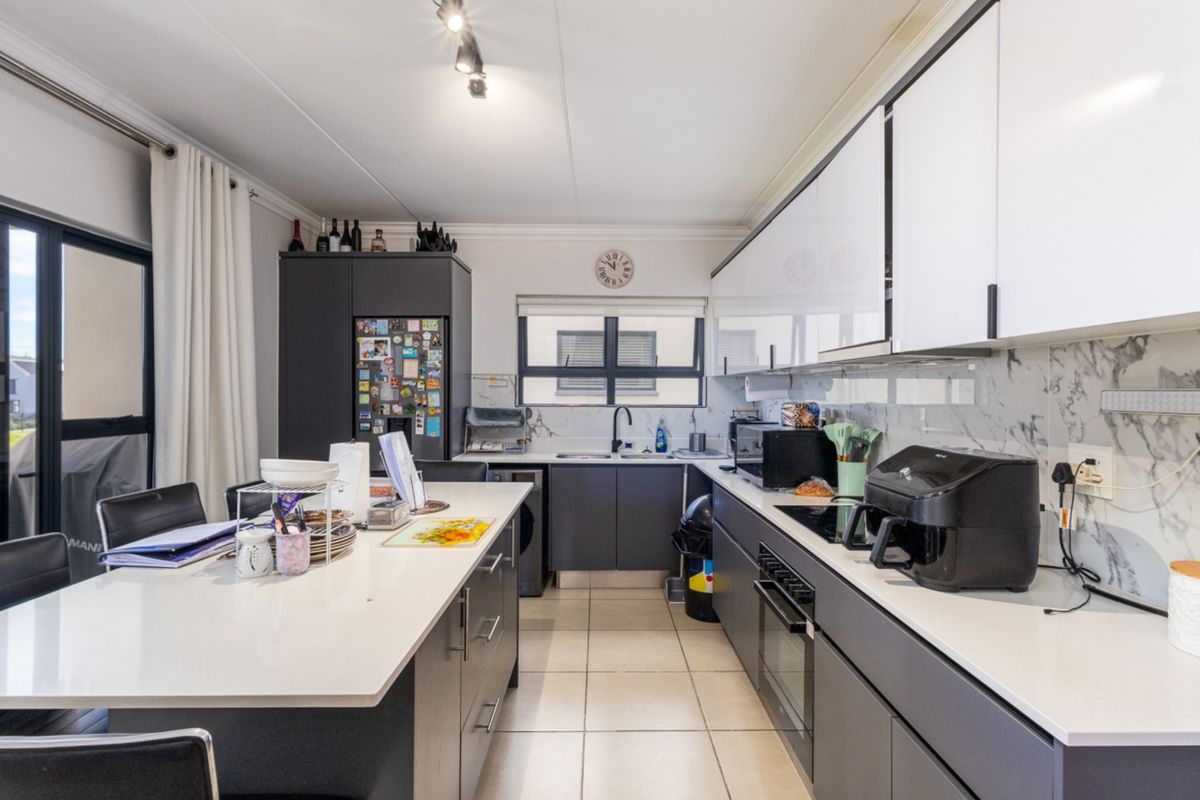 Modern kitchen featuring a central island, sleek dark cabinetry, marble-look splashback, built-in oven, and ceramic hob with tiled flooring.
