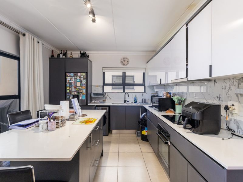 Modern kitchen featuring a central island, sleek dark cabinetry, marble-look splashback, built-in oven, and ceramic hob with tiled flooring.