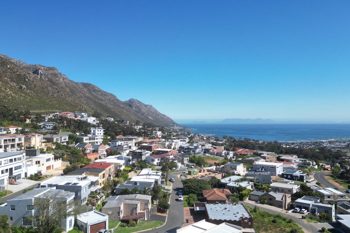 An elevated aerial view showcasing the coastal residential neighbourhood, surrounding mountain range, and ocean horizon.