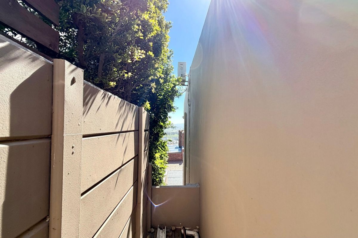 A narrow side passage between the property wall and a boundary fence, featuring an external air conditioning unit.