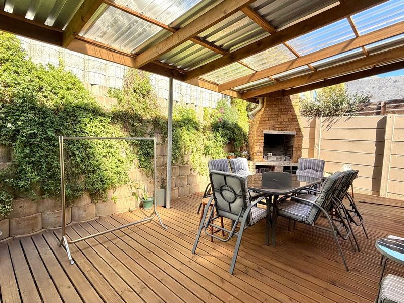 A covered outdoor patio featuring timber decking and a built-in brick braai, perfect for alfresco dining and entertaining.