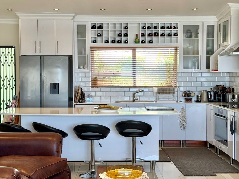 Modern kitchen featuring white cabinetry, subway tile backsplash, quartz countertops, built-in wine storage, and integrated stainless steel appliances.