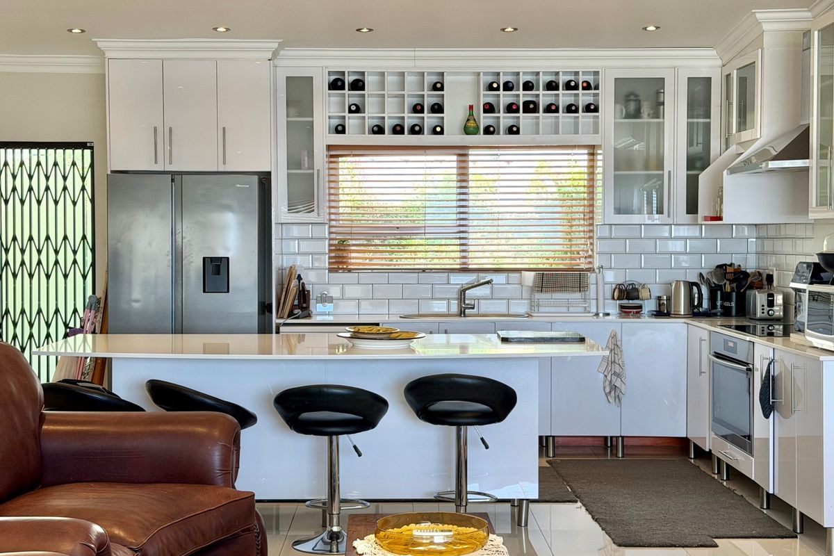 Modern kitchen featuring white cabinetry, subway tile backsplash, quartz countertops, built-in wine storage, and integrated stainless steel appliances.