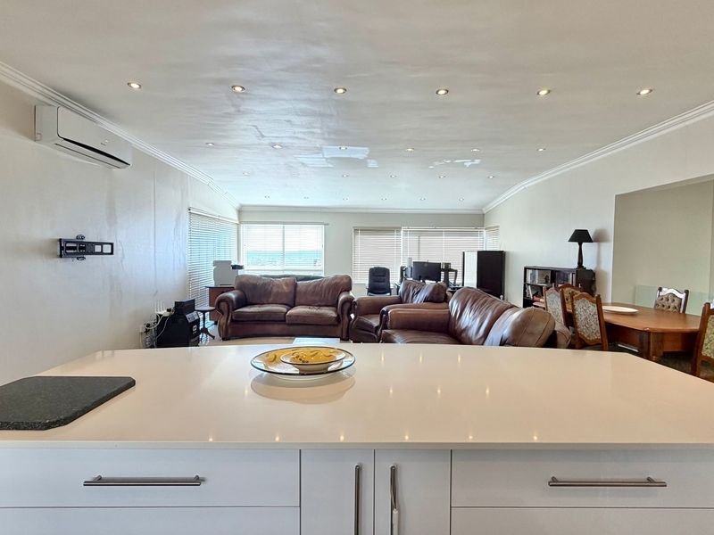Spacious open-plan living area featuring a modern kitchen island with quartz countertops, recessed lighting, and integrated air conditioning, creating a bright, functional living space.