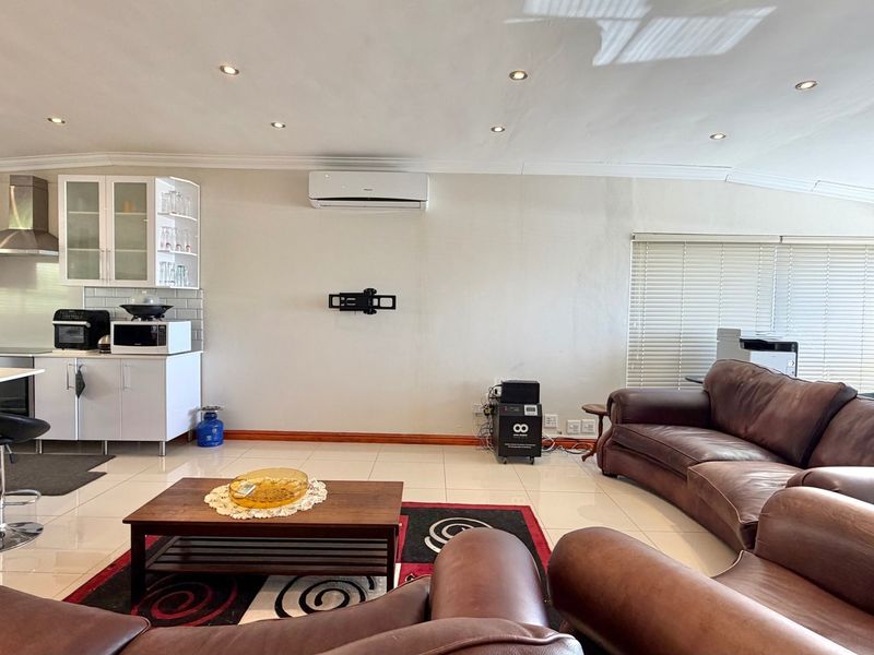 Spacious open-plan living area featuring a modern kitchen with subway tile backsplash, recessed lighting, and a wall-mounted air conditioning unit.
