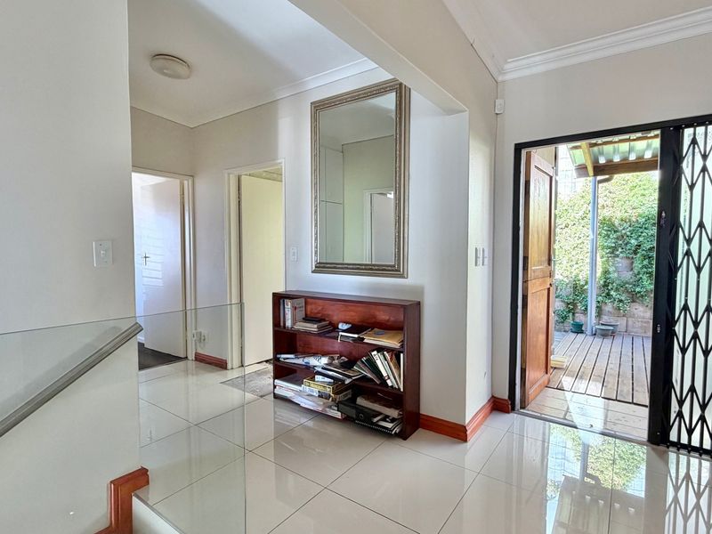 Bright entrance hall featuring polished tiled flooring, a modern glass balustrade, and direct access to an outdoor patio area through a security gate.