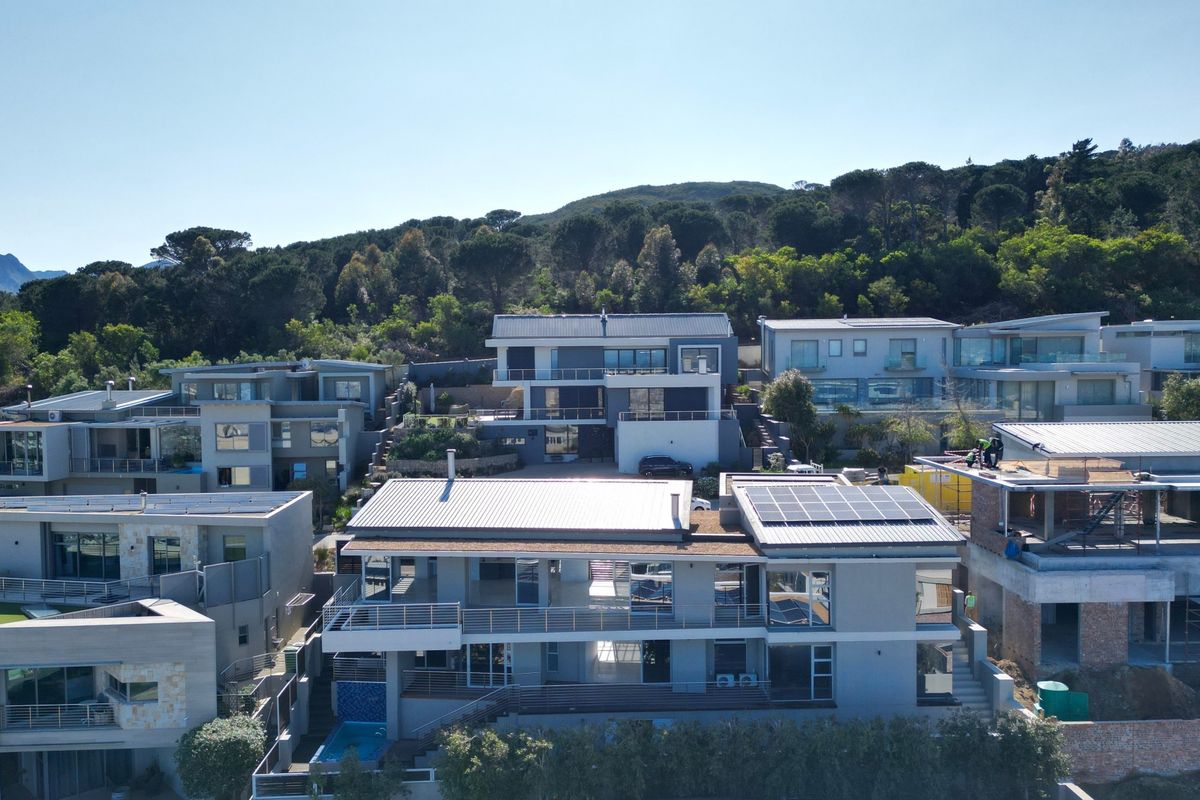Aerial view of a modern residential estate featuring multi-level homes with metal roofs, solar panels, and private swimming pools.