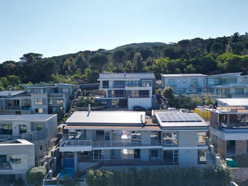Aerial view of a modern residential estate featuring multi-level homes with metal roofs, solar panels, and private swimming pools.