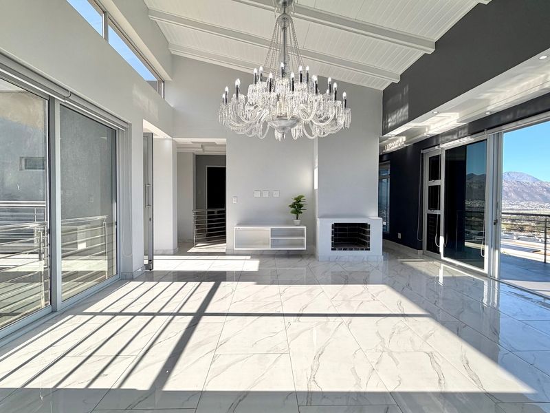 Spacious, light-filled living area featuring vaulted ceilings, marble-look tiled flooring, a built-in fireplace, and expansive sliding glass doors opening to a scenic balcony.