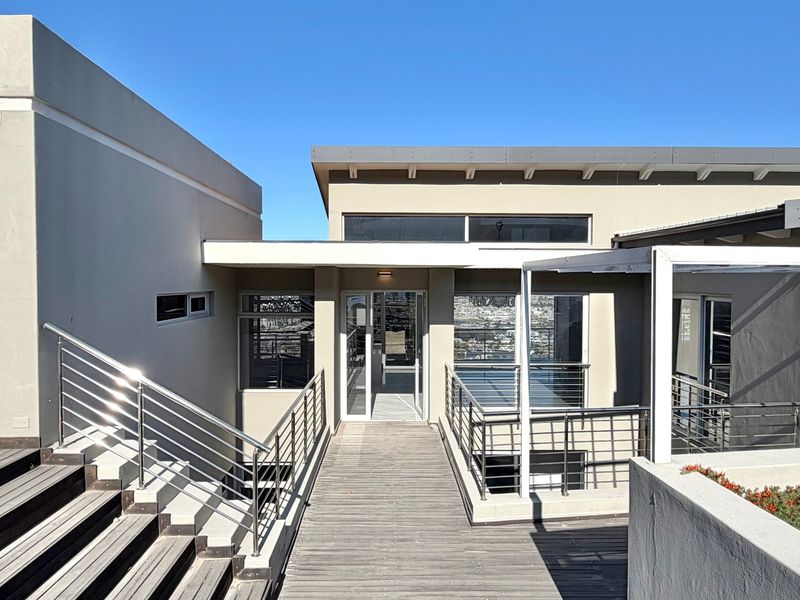 Modern architectural entrance featuring a raised timber walkway, stainless steel balustrades, and a glass front door with clean, contemporary lines.