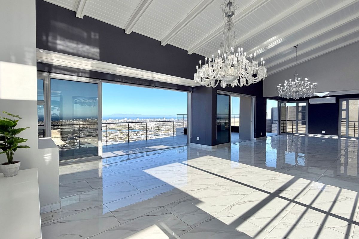 Spacious open-plan living area featuring high vaulted ceilings, polished marble-look flooring, elegant crystal chandeliers, and expansive sliding doors opening to a panoramic city view.