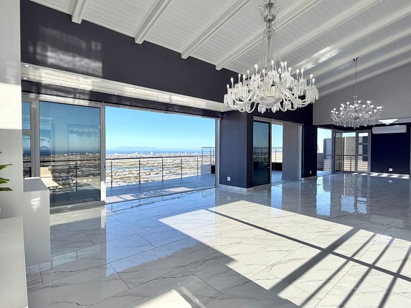 Spacious open-plan living area featuring high vaulted ceilings, polished marble-look flooring, elegant crystal chandeliers, and expansive sliding doors opening to a panoramic city view.
