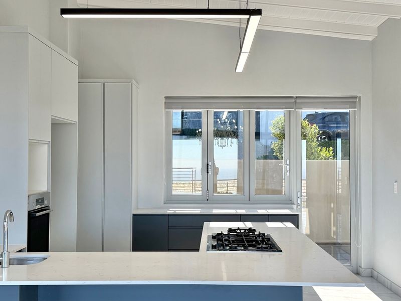 A modern, minimalist kitchen featuring sleek cabinetry, stone countertops, a built-in gas hob, and an integrated oven, illuminated by contemporary linear lighting.