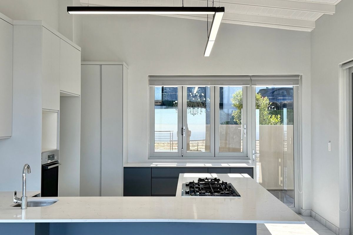 A modern, minimalist kitchen featuring sleek cabinetry, stone countertops, a built-in gas hob, and an integrated oven, illuminated by contemporary linear lighting.
