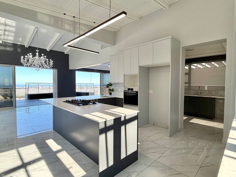 Modern open-plan kitchen and living area featuring a central island, sleek cabinetry, marble-look flooring, and expansive sliding doors leading to a balcony with views.