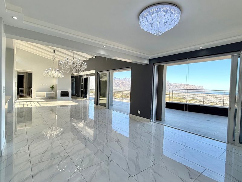 Spacious open-plan living area featuring polished marble-look floor tiles, elegant crystal chandeliers, and large sliding doors opening to a balcony with mountain views.