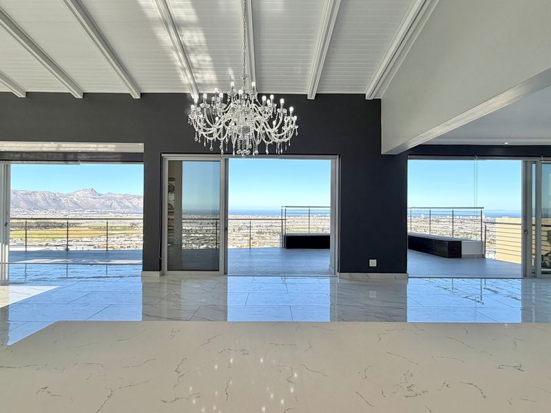 Spacious open-plan living area featuring high-end marble-look tiles, exposed beam ceilings, and expansive sliding doors opening to a balcony with panoramic mountain and city views.