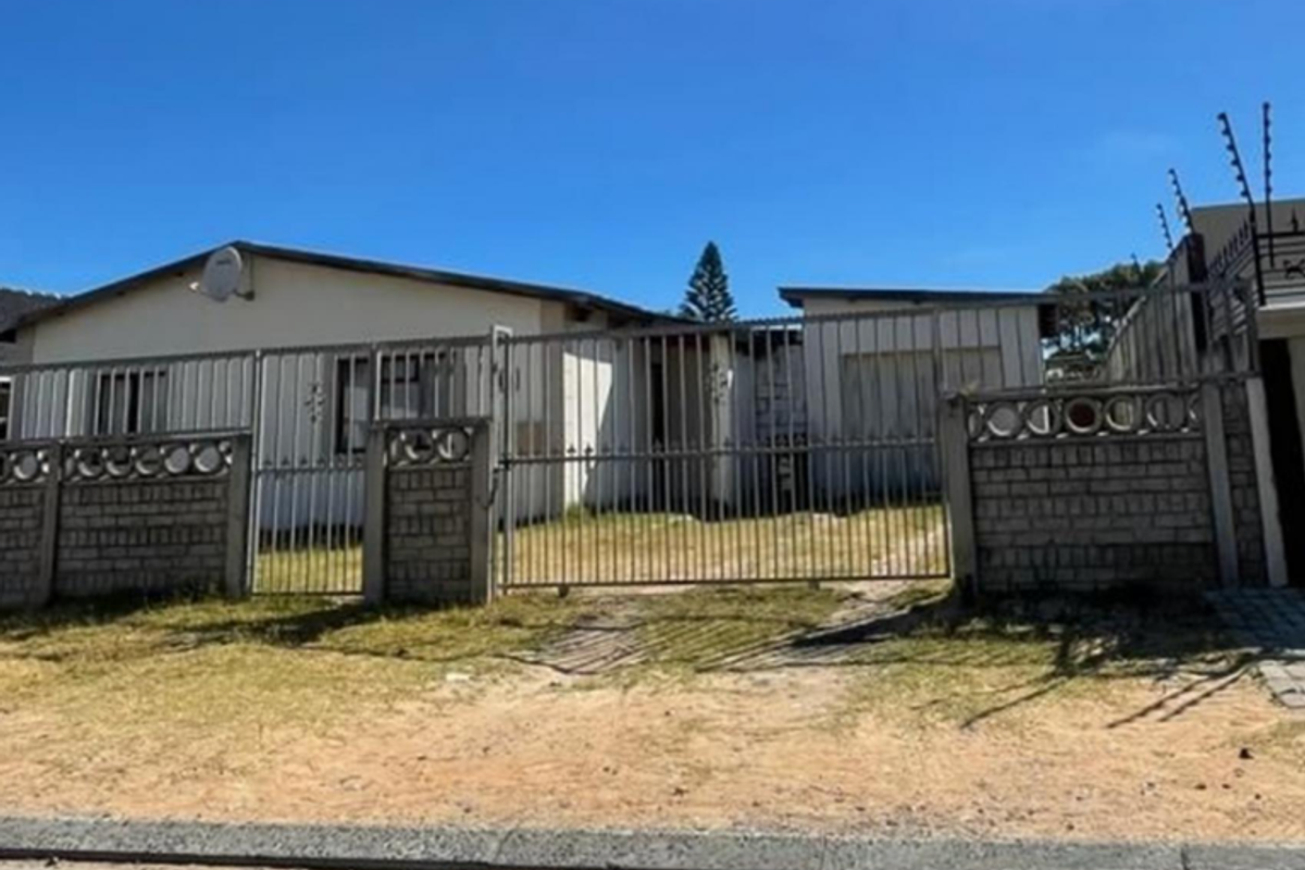 Front view of a single-story house featuring a secure metal gate, brick boundary wall with electric fencing, and an attached garage.