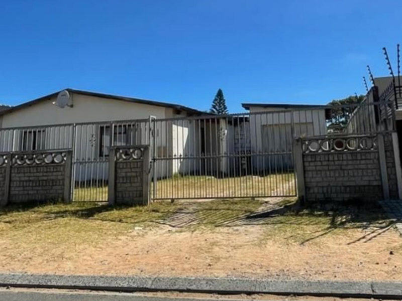 Front view of a single-story house featuring a secure metal gate, brick boundary wall with electric fencing, and an attached garage.