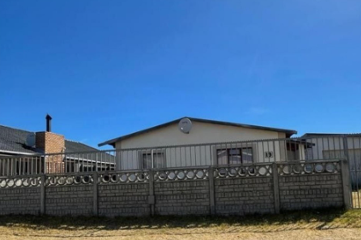 Front exterior view of a residential property featuring a perimeter concrete block wall, metal security fencing, and a satellite dish.