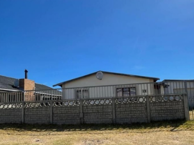 Front exterior view of a residential property featuring a perimeter concrete block wall, metal security fencing, and a satellite dish.