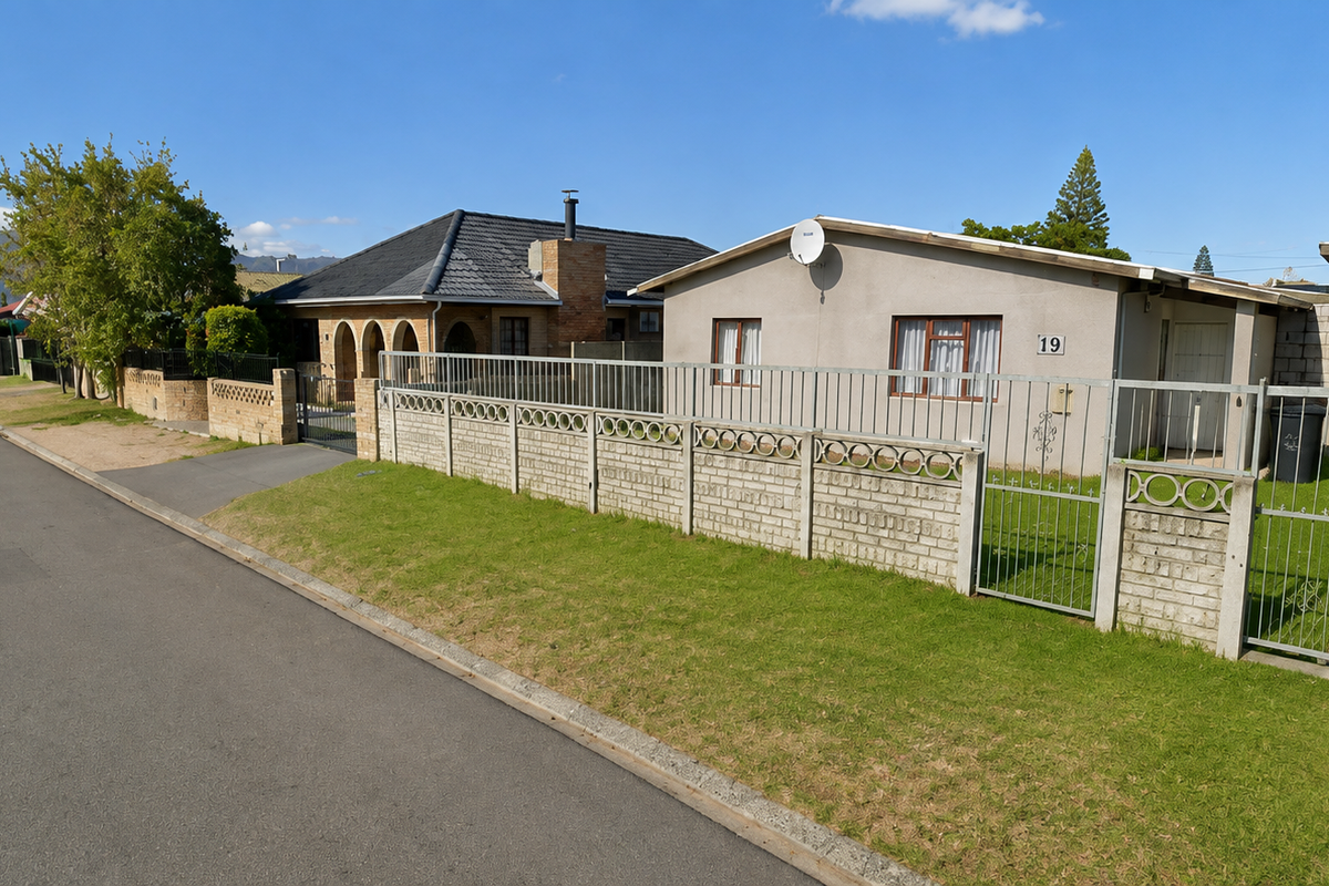 Street view of a residential property featuring a concrete perimeter wall, metal security fencing, and a single garage.