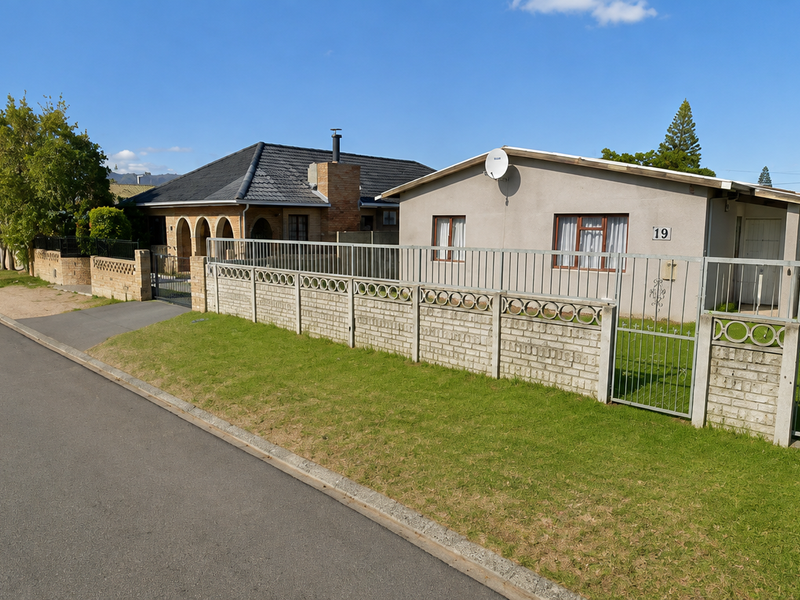 Street view of a residential property featuring a concrete perimeter wall, metal security fencing, and a single garage.