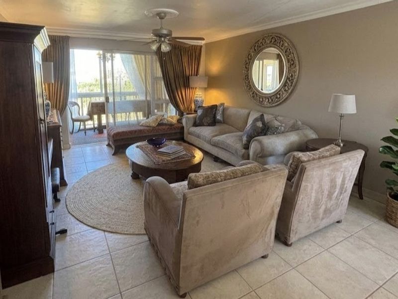 A comfortable living room featuring tiled flooring, a ceiling fan, and large sliding glass doors that provide access to an outdoor balcony area.