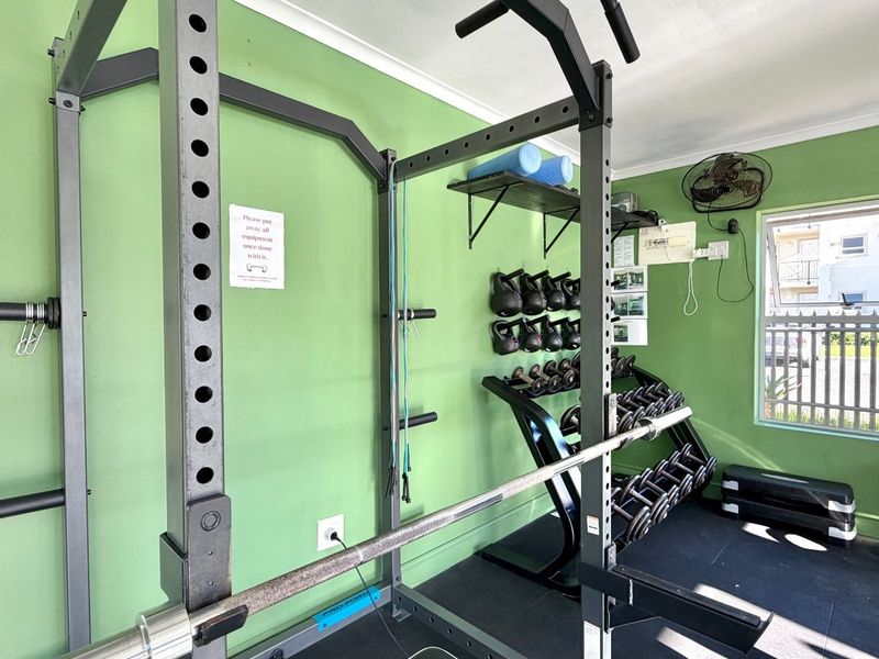 A functional gym space featuring rubber flooring, wall-mounted shelving, and a wall-mounted fan, providing a dedicated area for fitness activities.