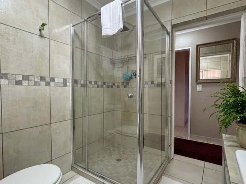 A well-maintained bathroom featuring a glass-enclosed shower, neutral wall tiling with decorative accents, and a functional vanity area.