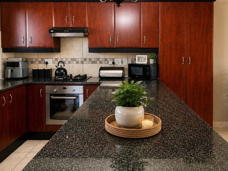 A well-maintained kitchen featuring dark wood cabinetry, granite countertops, a built-in oven, gas hob, and a functional breakfast bar layout.