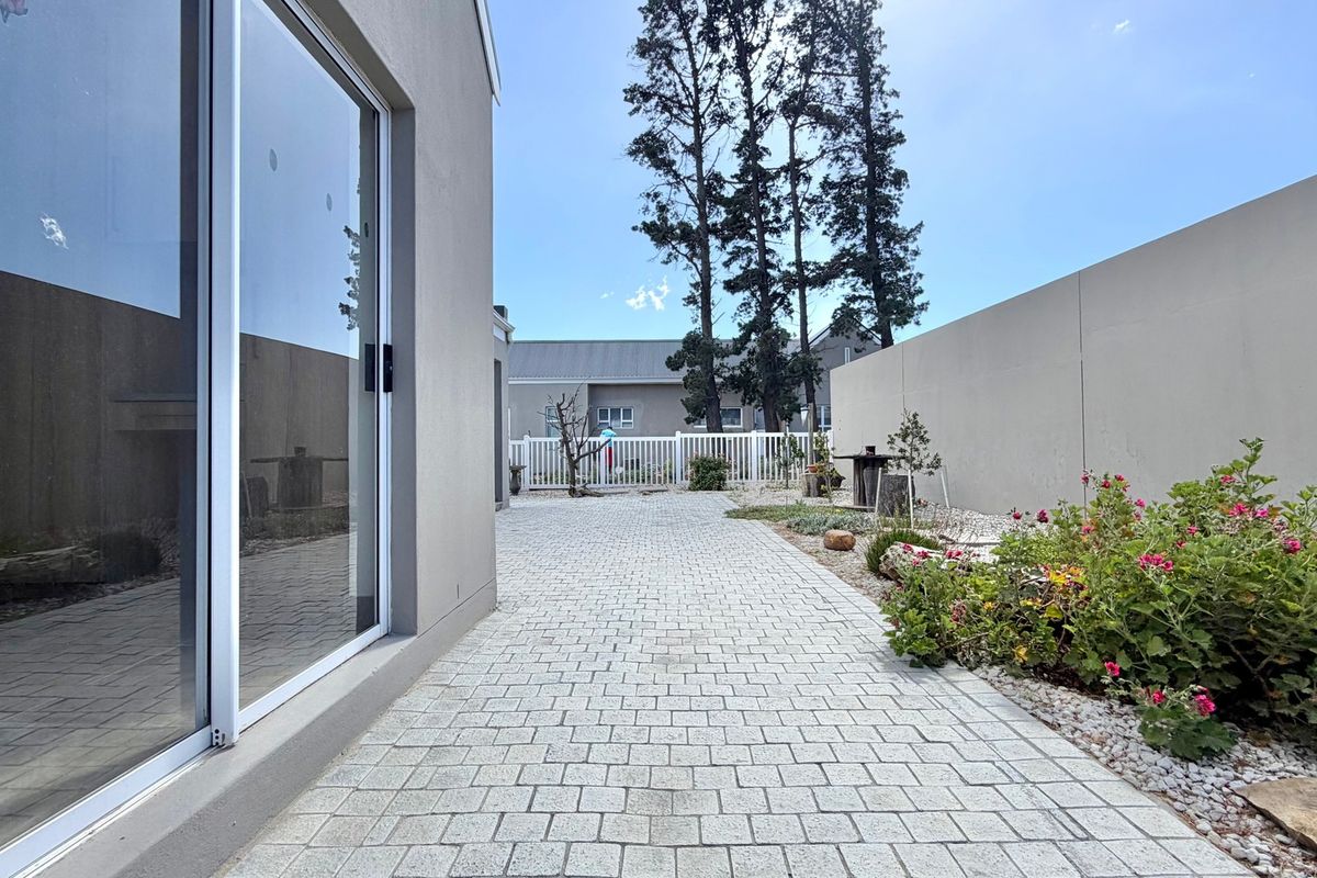A well-maintained rear exterior area featuring a paved patio, boundary walls, and a white picket fence, providing a clean and private outdoor space.
