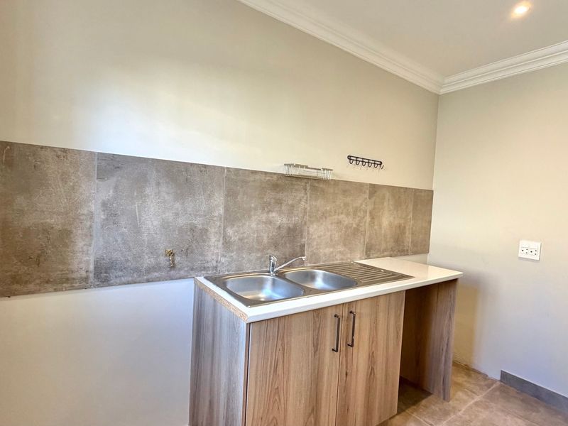 A clean and functional laundry area featuring a double bowl stainless steel sink, modern laminate cabinetry, and a stylish stone-look tiled splashback.