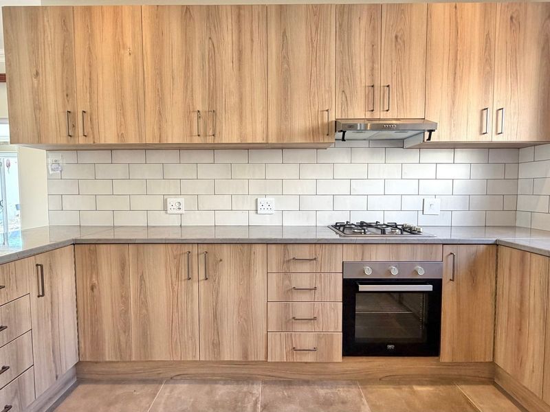 Modern kitchen featuring light wood-grain cabinetry, subway tile backsplash, stone countertops, and integrated stainless steel appliances including a gas hob and oven.