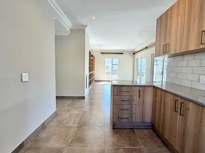 An open-plan living and kitchen area featuring modern wood-finish cabinetry, stone countertops, subway tile backsplash, and large sliding doors leading to the exterior.