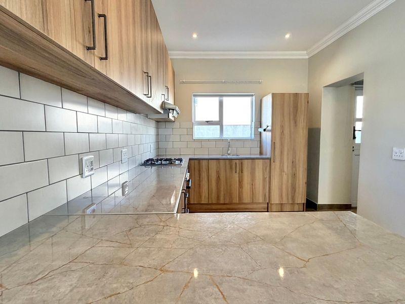 Modern kitchen featuring wood-finish cabinetry, stone countertops, subway tile backsplash, and integrated gas hob with extractor fan.
