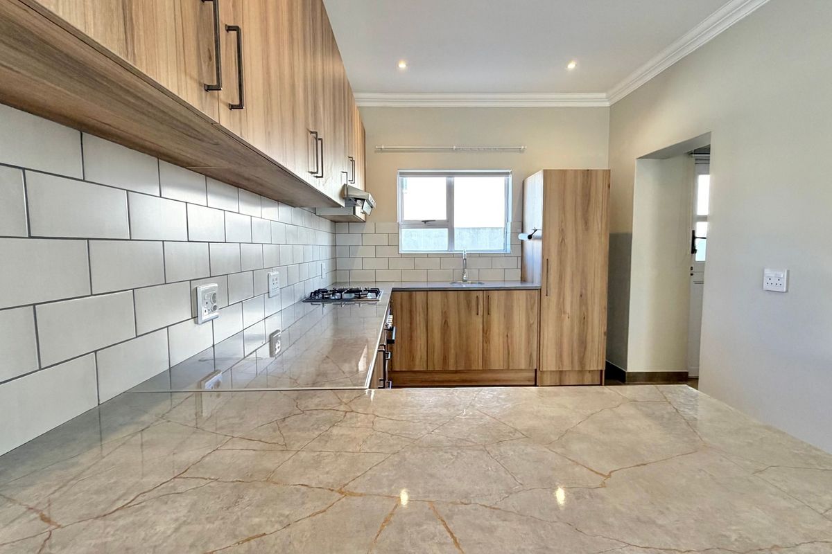 Modern kitchen featuring wood-finish cabinetry, stone countertops, subway tile backsplash, and integrated gas hob with extractor fan.