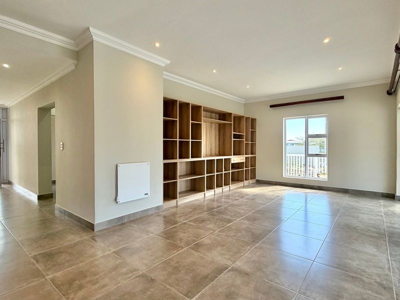 Spacious living area featuring neutral tiled flooring, recessed lighting, and a large built-in wooden shelving unit, with direct access to outdoor space.