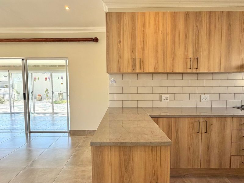 Modern open-plan kitchen featuring wood-look cabinetry, stone countertops, and subway tile backsplash, flowing seamlessly to an outdoor patio area through sliding glass doors.