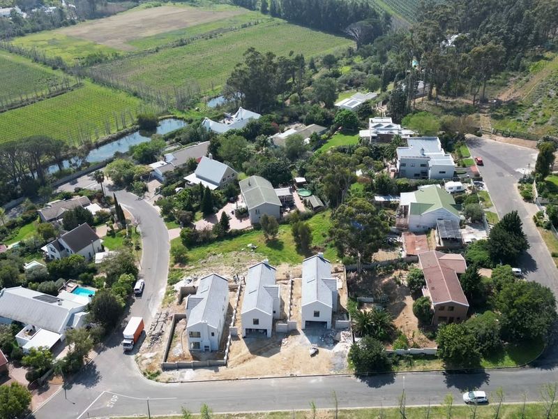 An aerial view of a residential neighborhood featuring established homes, mature trees, and new construction plots in a scenic, semi-rural setting.