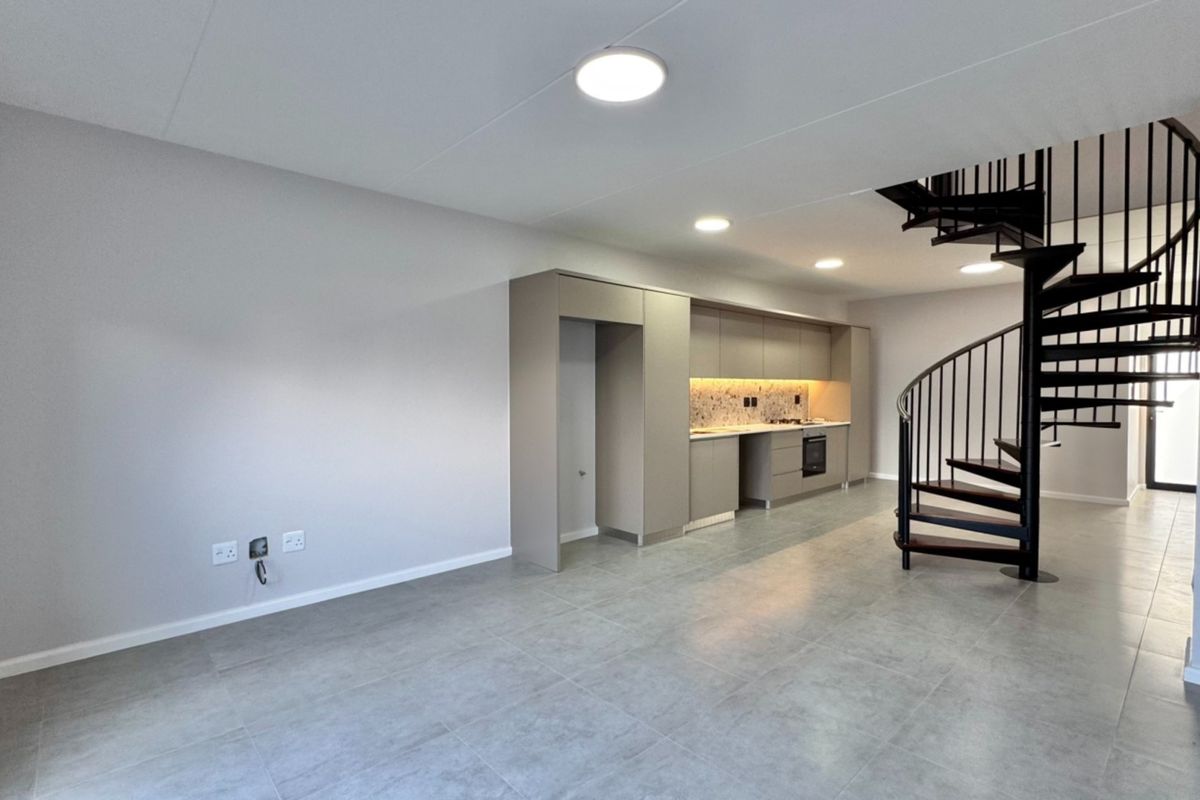 Modern open-plan living area featuring a sleek kitchen with built-in appliances, tiled flooring, and a striking black spiral staircase leading to the upper level.