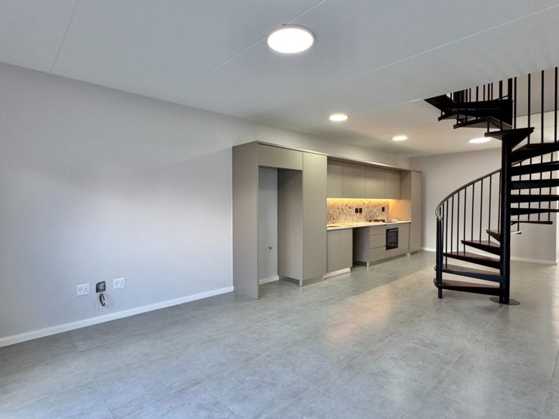 Modern open-plan living area featuring a sleek kitchen with built-in appliances, tiled flooring, and a striking black spiral staircase leading to the upper level.
