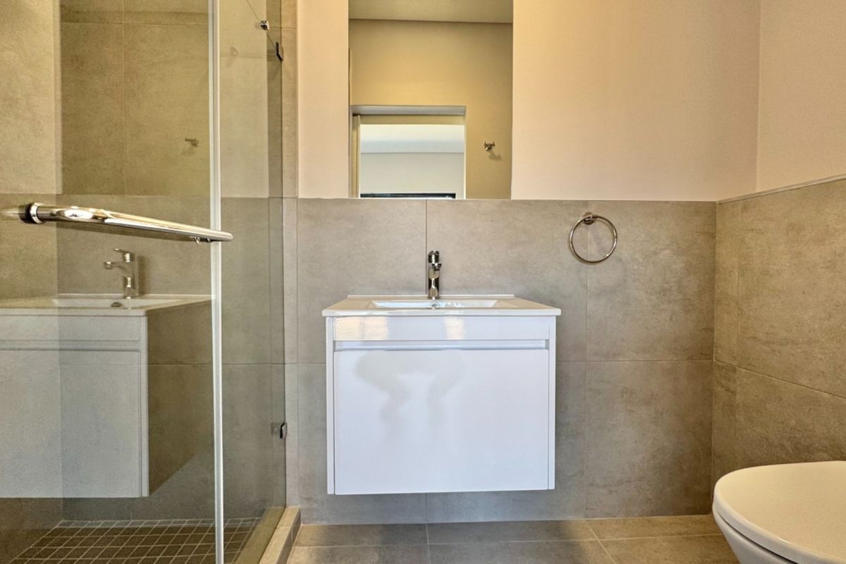 Modern bathroom featuring a wall-mounted vanity, glass shower enclosure, and neutral floor-to-ceiling tiling.