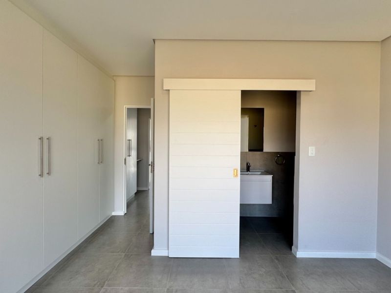 Spacious bedroom featuring modern tiled flooring, extensive built-in cupboards, and a contemporary sliding barn door leading to an en-suite bathroom.